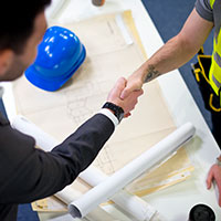 two men shaking hands over construction drafts